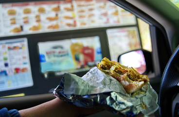 Half eaten cheeseburger in hand of hungry driver parked beside a